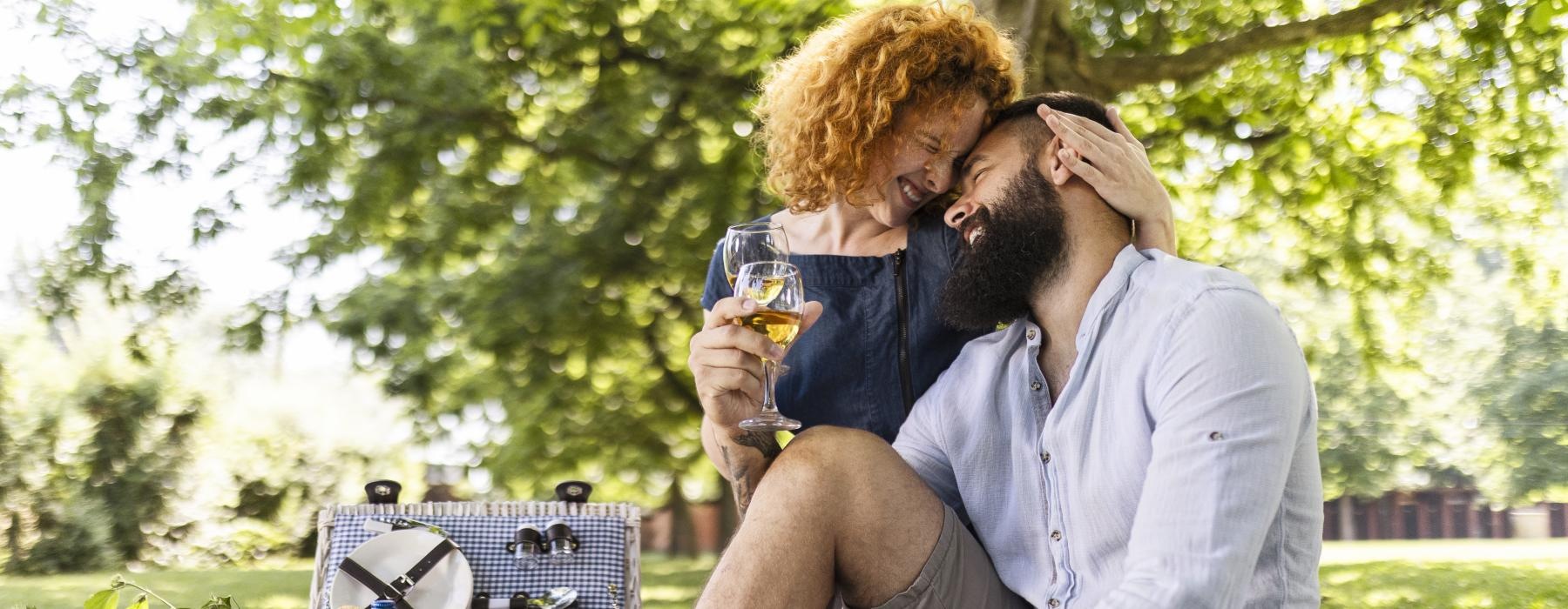 a man and woman sitting on a blanket with a basket of bread